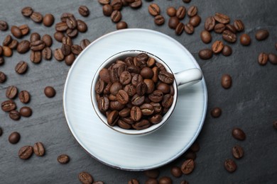 Cup with roasted coffee beans on black table, flat lay