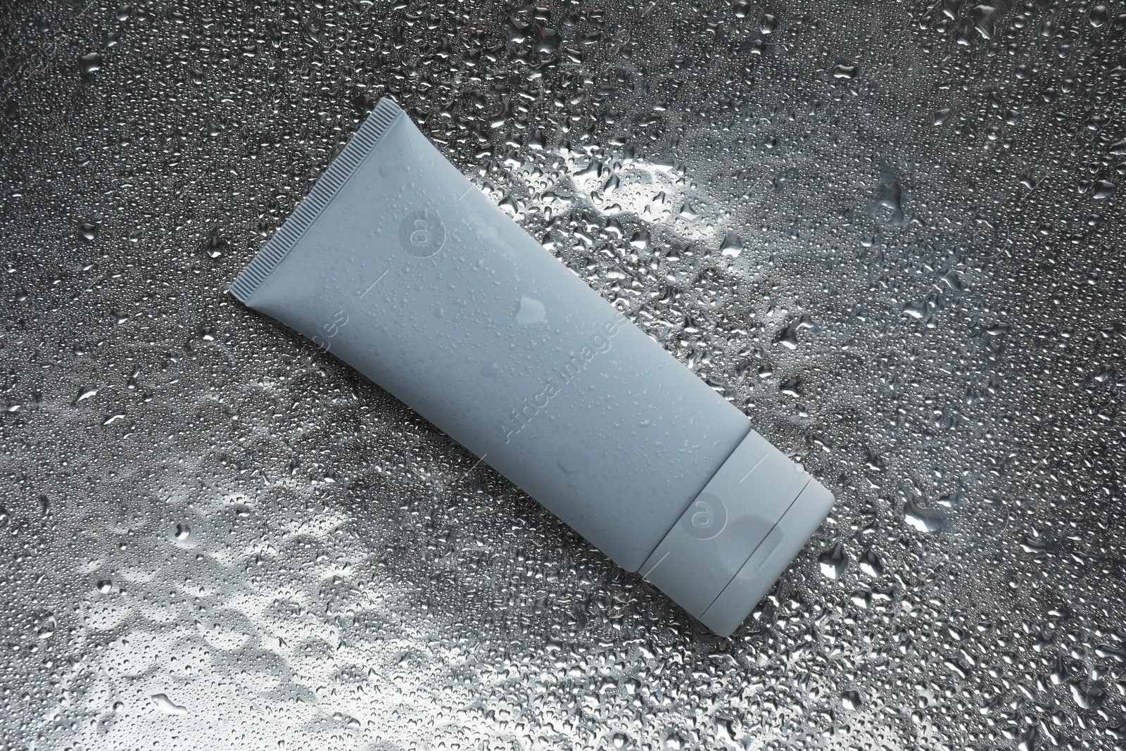 Photo of Moisturizing cream in tube on silver background with water drops, top view