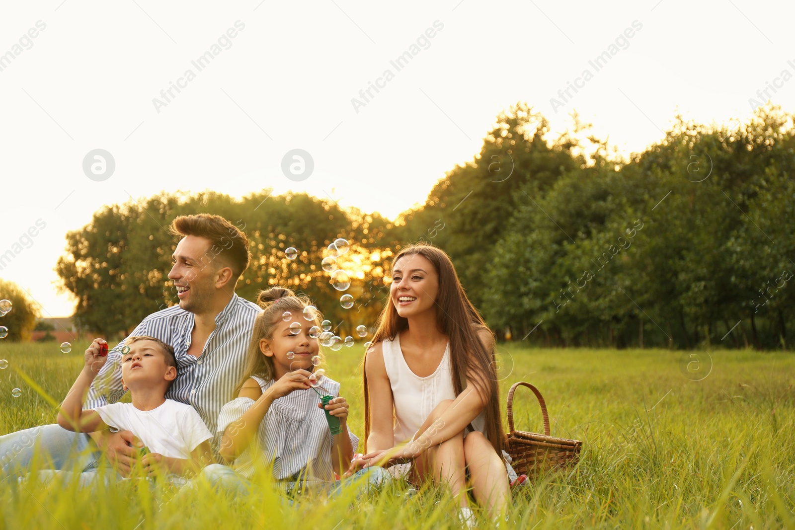 Photo of Happy family blowing soap bubbles in park at sunset. Summer picnic