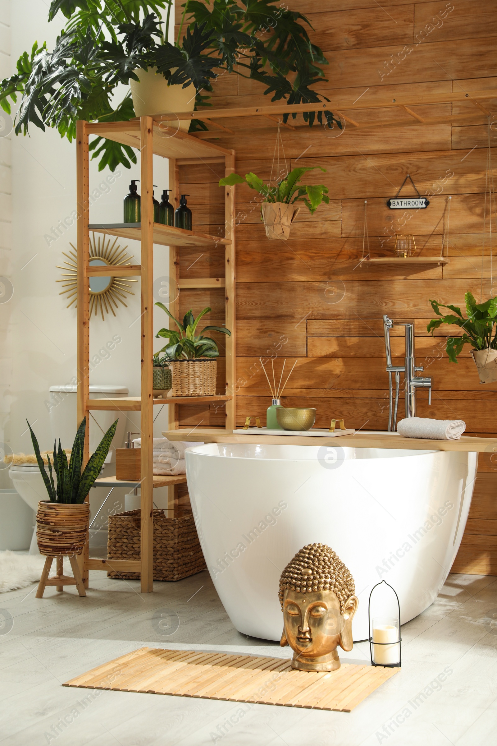 Photo of Stylish bathroom interior with white tub and green houseplants near wooden wall. Idea for design