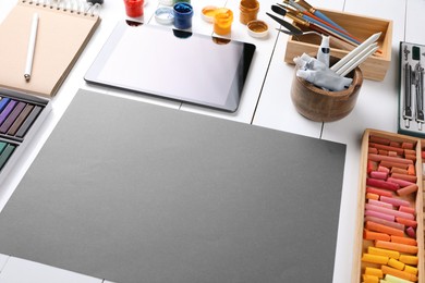 Photo of Blank sheet of paper, colorful chalk pastels, tablet and other drawing tools on white wooden table. Modern artist's workplace