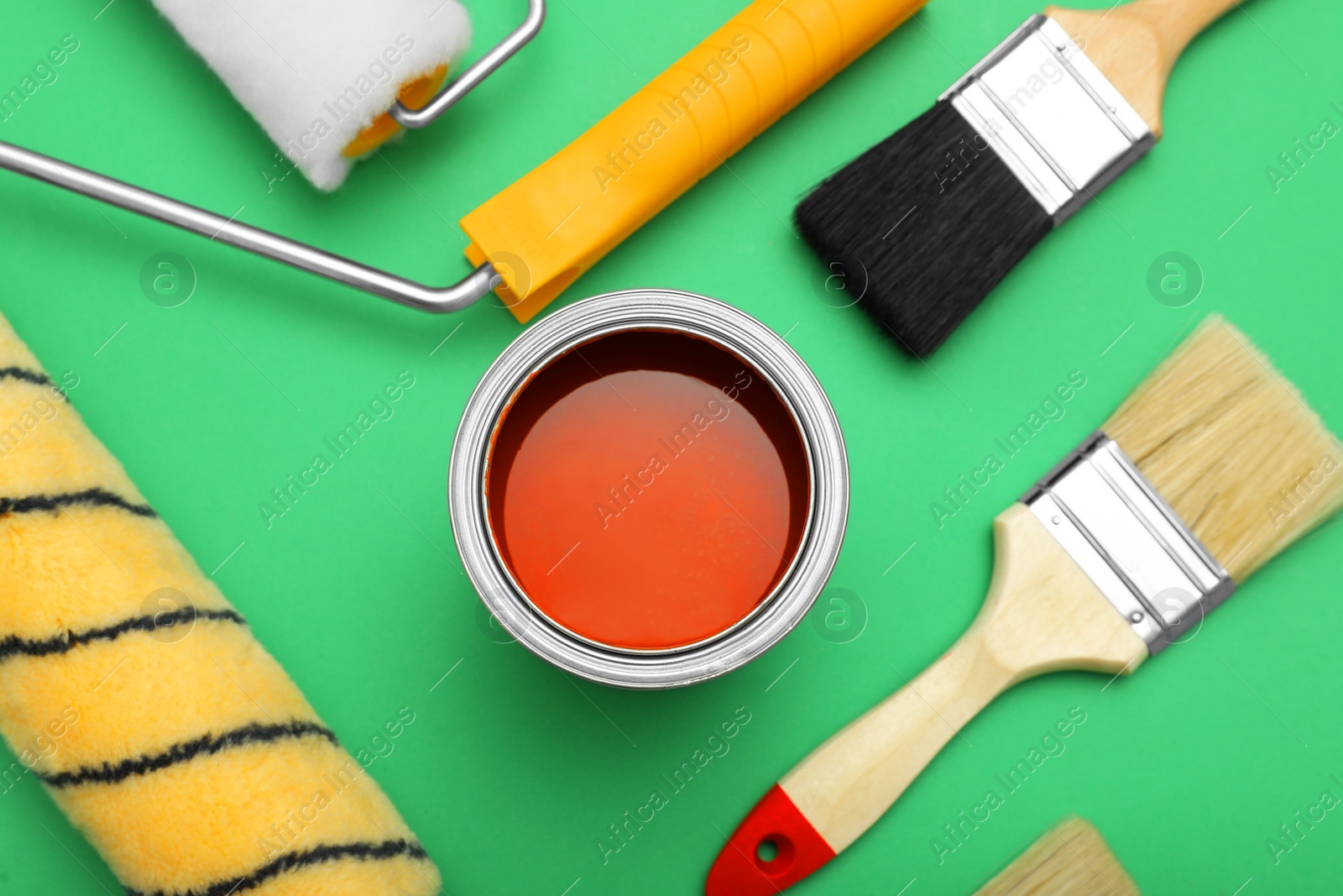 Photo of Can of orange paint, brushes and rollers on green background, flat lay