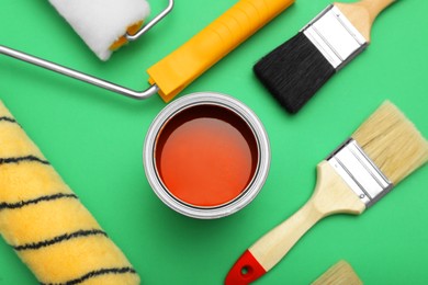 Photo of Can of orange paint, brushes and rollers on green background, flat lay