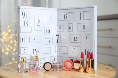 Photo of Advent calendar with different cosmetics and perfumes on wooden table against blurred lights. Presents for Christmas