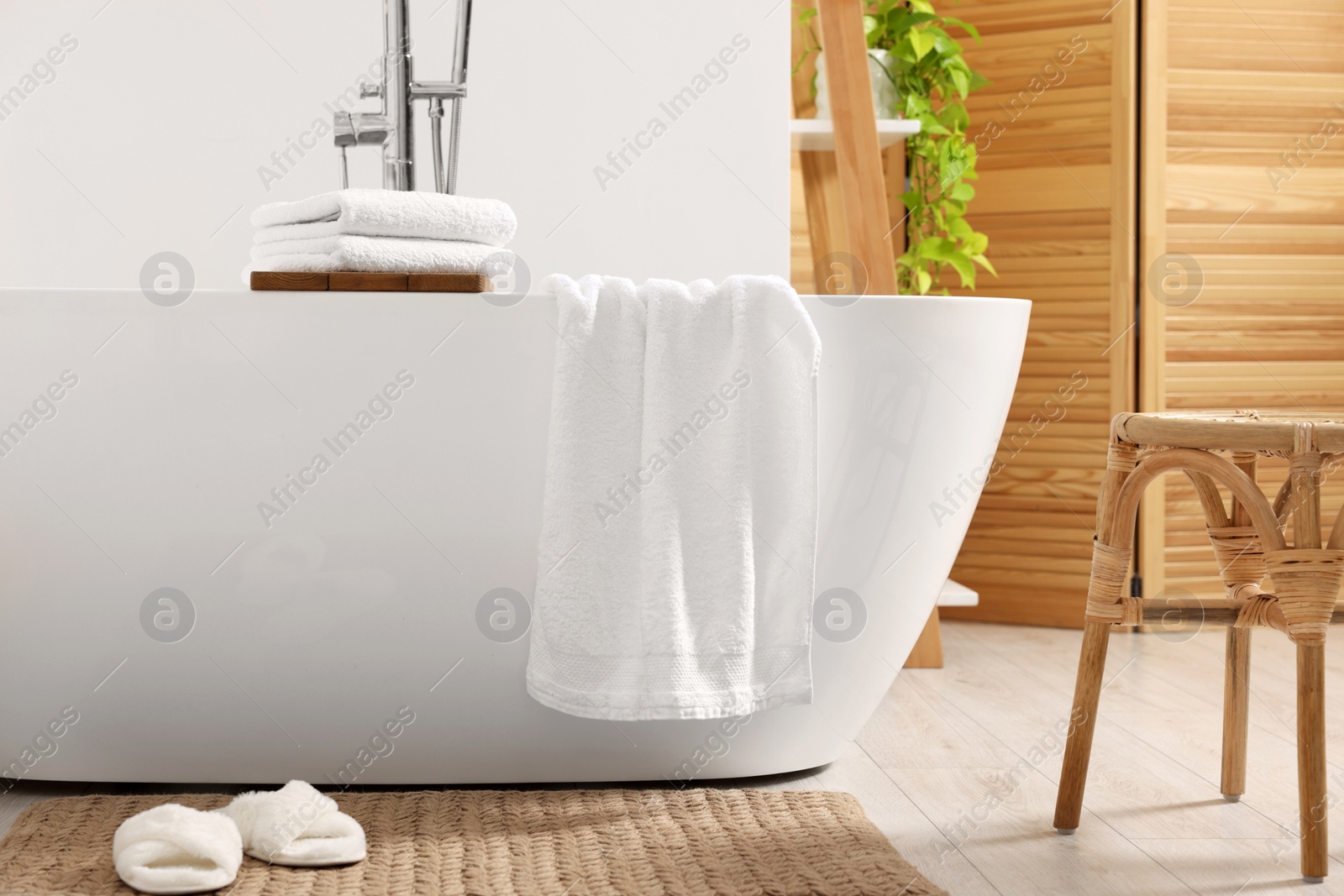 Photo of Stylish tub, wicker stool, slippers and soft towels in bathroom