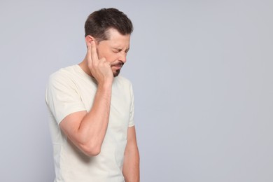 Man suffering from ear pain on grey background, space for text