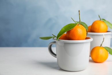 Fresh ripe tangerines with green leaves and mugs on table. Space for text