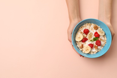 Photo of Woman holding bowl with oatmeal and fresh fruits on color background