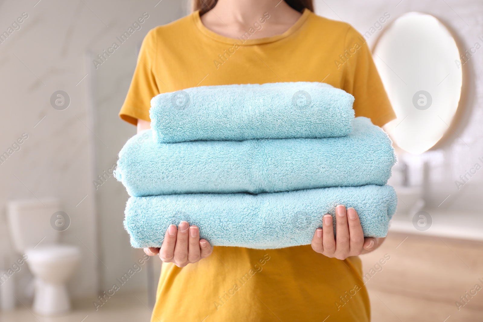 Photo of Woman holding stack of fresh towels indoors, closeup