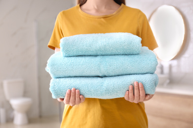 Photo of Woman holding stack of fresh towels indoors, closeup