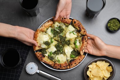 Photo of People taking slices of delicious pizza with pesto, cheese and basil at black table, top view