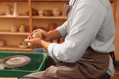 Photo of Man crafting with clay over potter's wheel indoors, closeup
