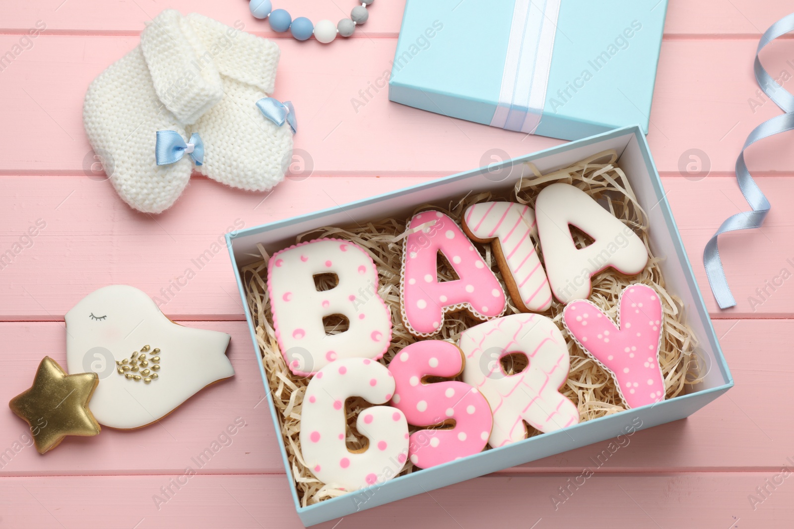 Photo of Set of baby shower cookies in gift box and accessories on pink wooden table, flat lay