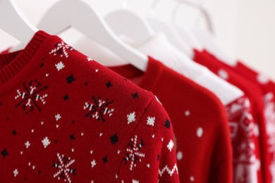 Different Christmas sweaters hanging on rack, closeup