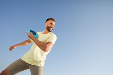 Happy man throwing flying disk against blue sky on sunny day, low angle view