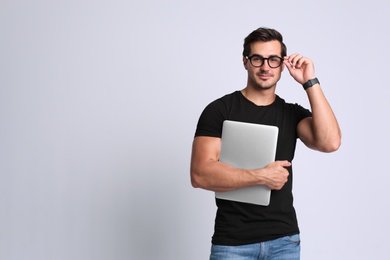 Photo of Handsome young man with laptop on grey background. Space for text