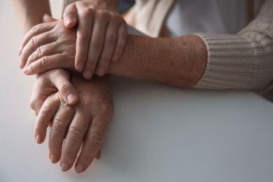 Young and elderly women holding hands together at white table, closeup