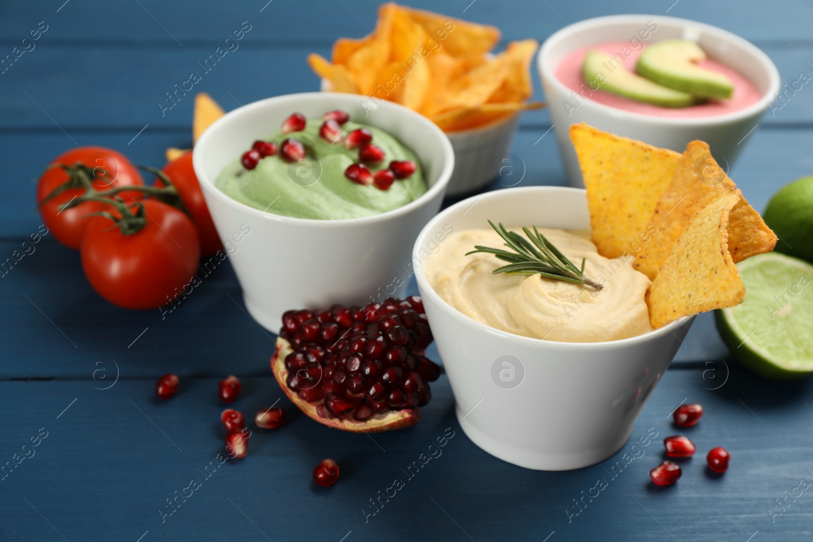 Photo of Different kinds of tasty hummus served with nachos on blue wooden table