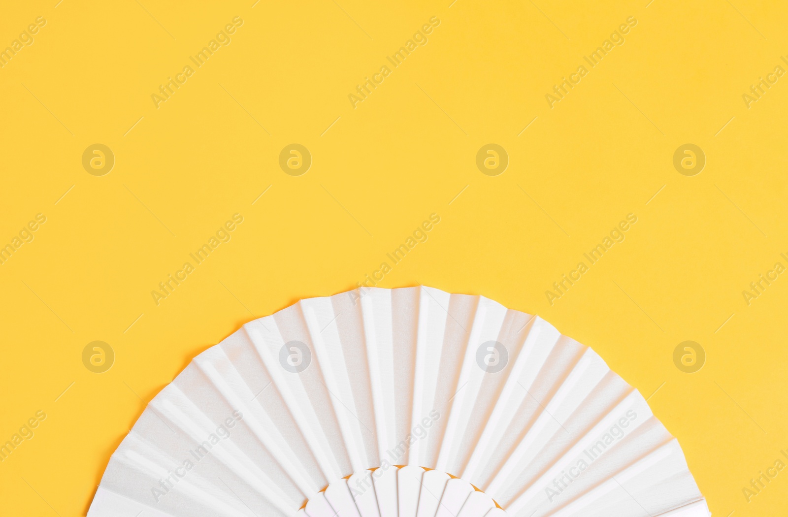 Photo of White hand fan on yellow background, top view. Space for text