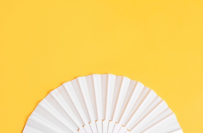 Photo of White hand fan on yellow background, top view. Space for text