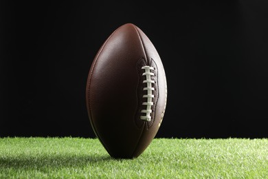 Photo of Leather American football ball on green grass against black background
