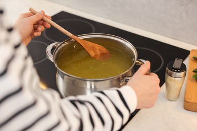 Photo of Woman with wooden spoon cooking soup in kitchen, closeup