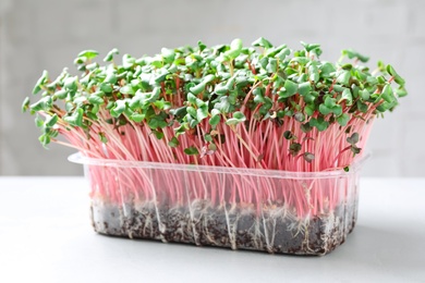 Photo of Fresh organic microgreen in plastic container on white table, closeup
