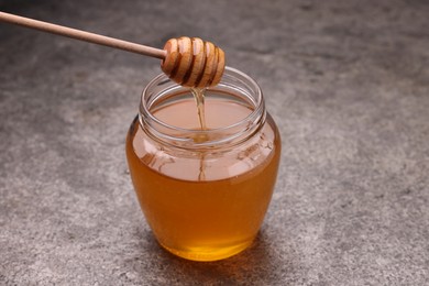 Photo of Pouring sweet golden honey from dipper into jar at grey textured table