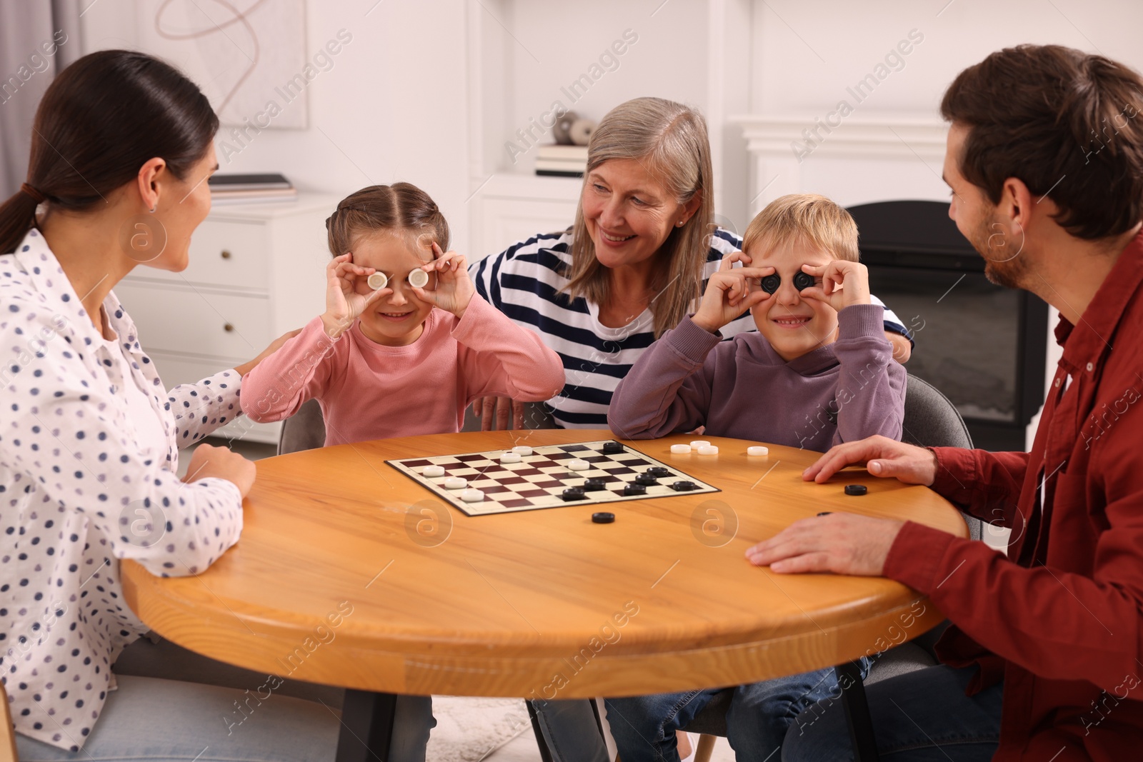 Photo of Children having fun while playing checkers with their family at wooden table in room