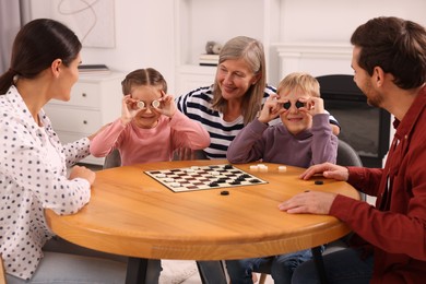Children having fun while playing checkers with their family at wooden table in room