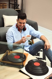 Photo of Happy man drinking tea while listening to music with turntable at home