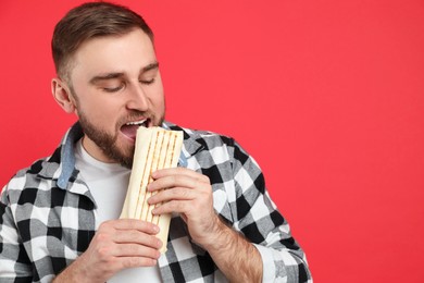 Young man eating delicious shawarma on red background, space for text