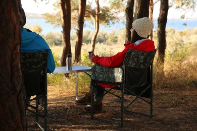 Young woman resting in camping chair and enjoying hot drink outdoors