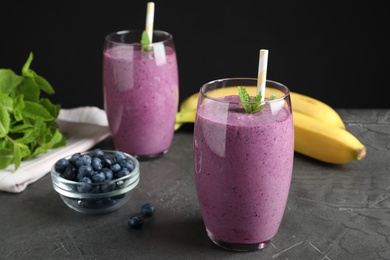 Photo of Glasses of delicious blueberry smoothie on grey table against black background