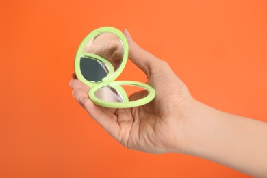 Woman holding stylish cosmetic pocket mirror on orange background, closeup