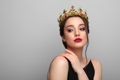 Beautiful young woman wearing luxurious crown on light grey background, space for text