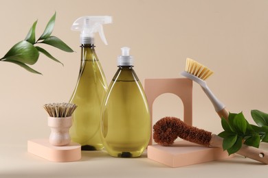 Bottles of cleaning product, brushes and floral decor on beige background