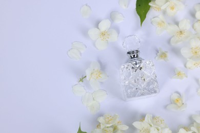 Aromatic perfume in bottle and beautiful jasmine flowers on white background, flat lay. Space for text