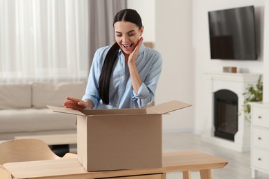 Photo of Emotional young woman with opened parcel at home. Internet shopping