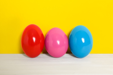 Photo of Easter eggs on white wooden table against yellow background