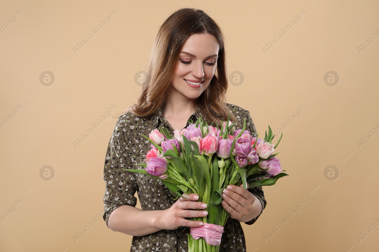 Photo of Happy young woman holding bouquet of beautiful tulips on beige background