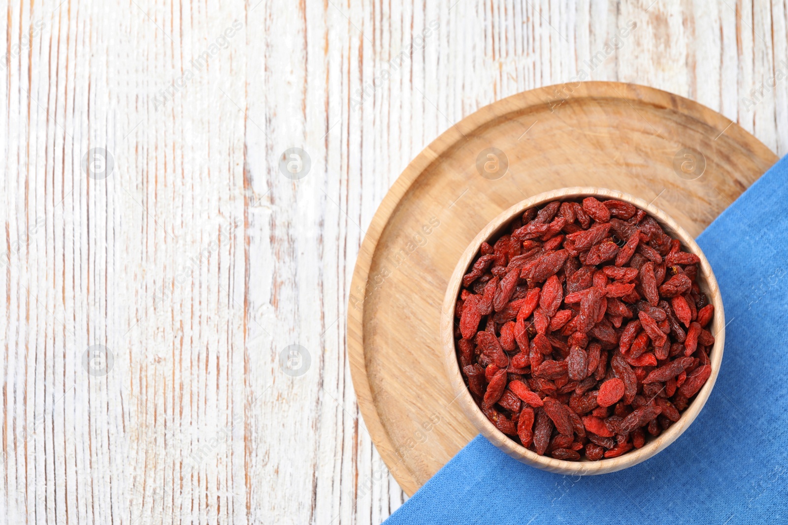 Photo of Dried goji berries in bowl on white wooden table, flat lay. Space for text