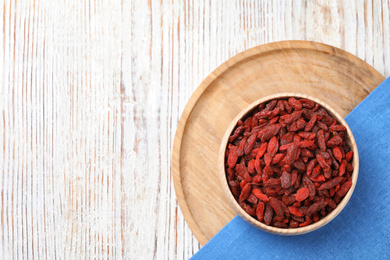 Photo of Dried goji berries in bowl on white wooden table, flat lay. Space for text