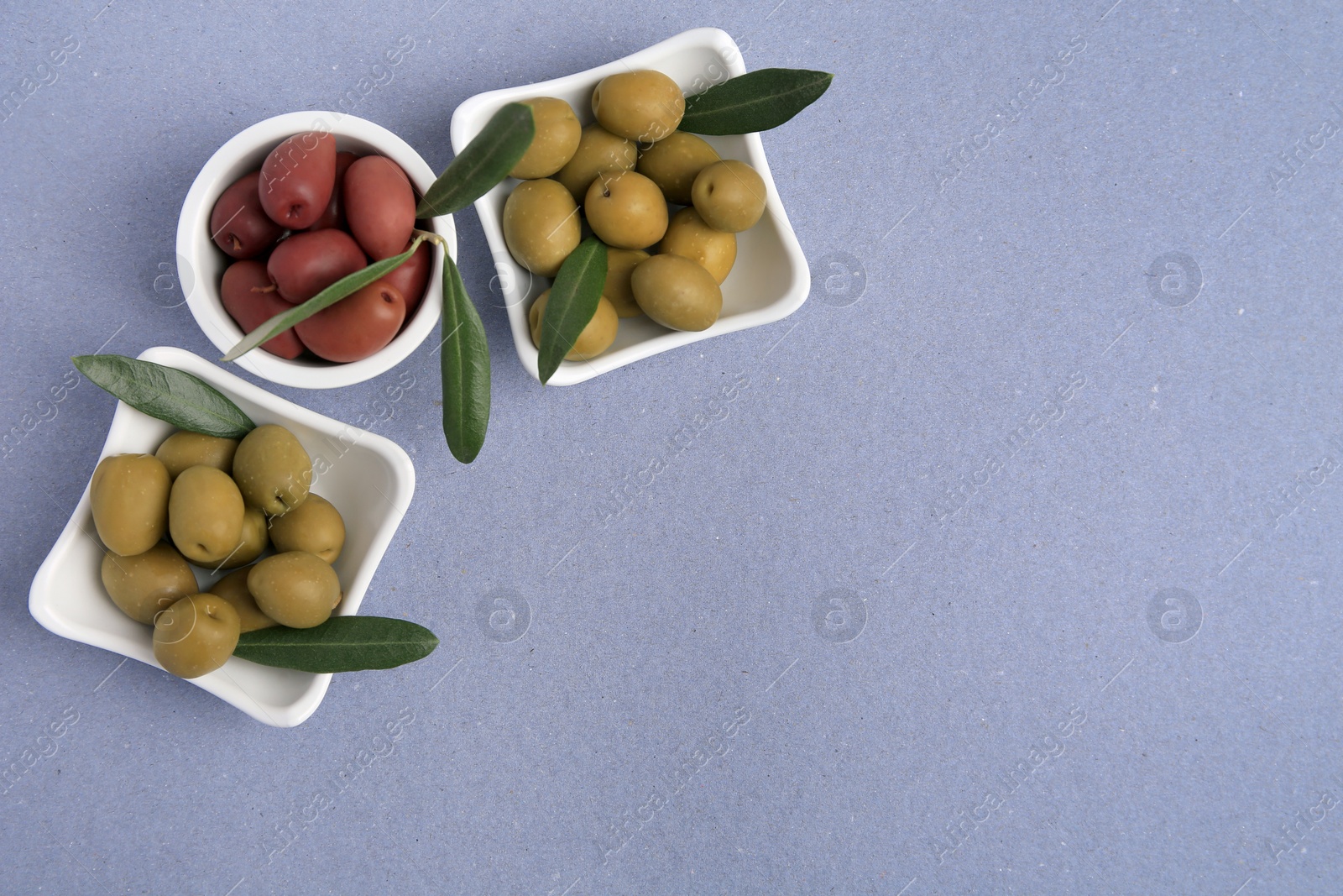 Photo of Different fresh olives and leaves on violet background, flat lay. Space for text