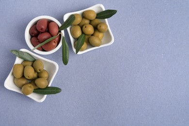 Different fresh olives and leaves on violet background, flat lay. Space for text