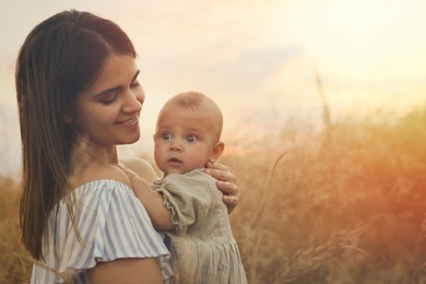 Happy mother with adorable baby in field at sunset, space for text