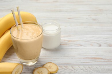 Glass of tasty banana smoothie with straws and ingredients on white wooden table. Space for text