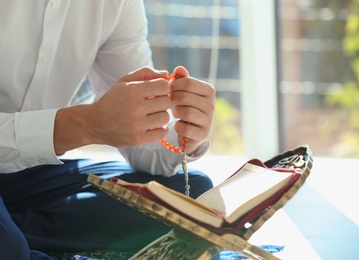 Photo of Muslim man with Koran and misbaha praying indoors, closeup