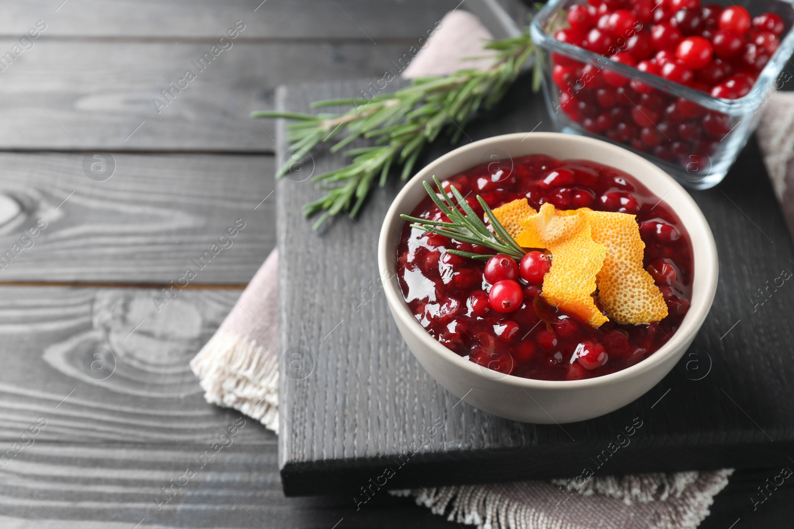 Photo of Fresh cranberry sauce, rosemary and orange peel in bowl on black wooden table, closeup. Space for text