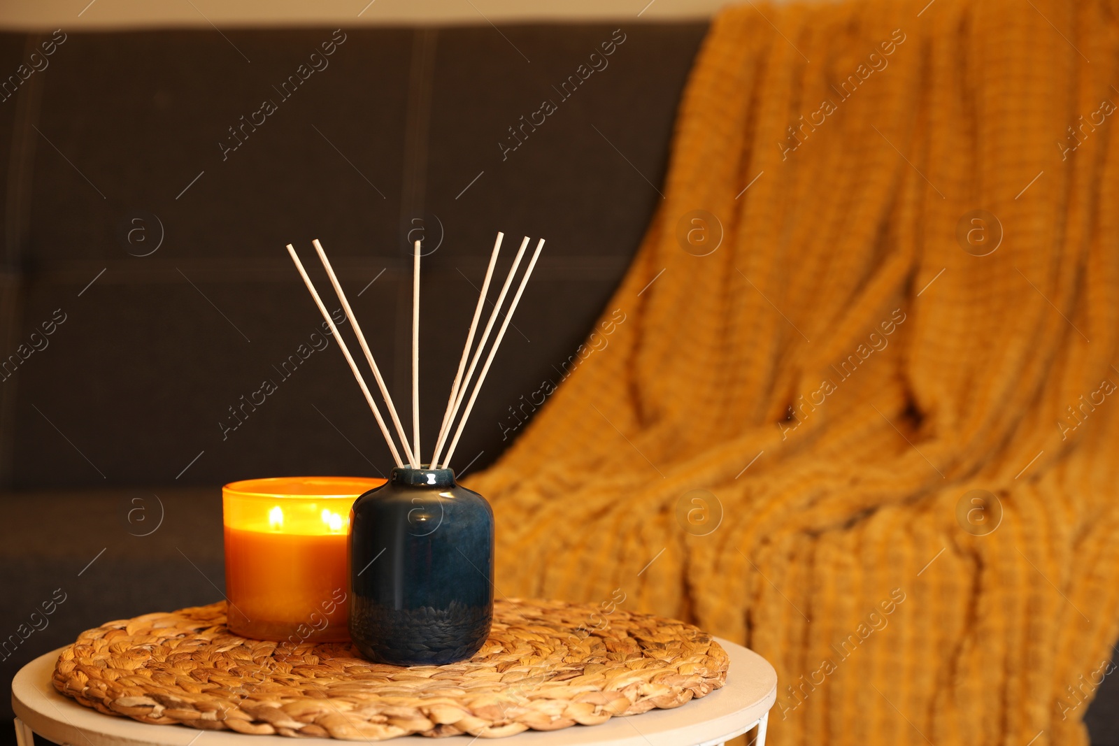 Photo of Aromatic reed air freshener and scented candle on table indoors, space for text